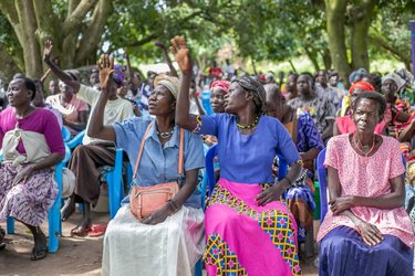 Seated women looking to the sky under trees in Uganda
